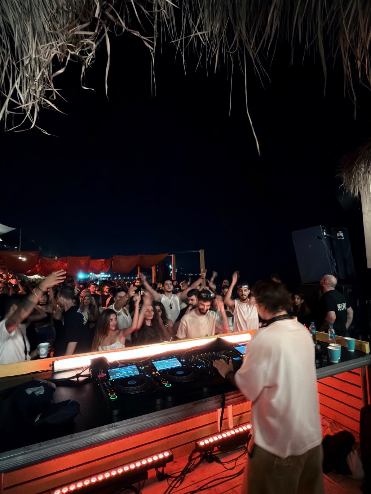 A DEEN in a white tee at a beach booth, crowd with hands up